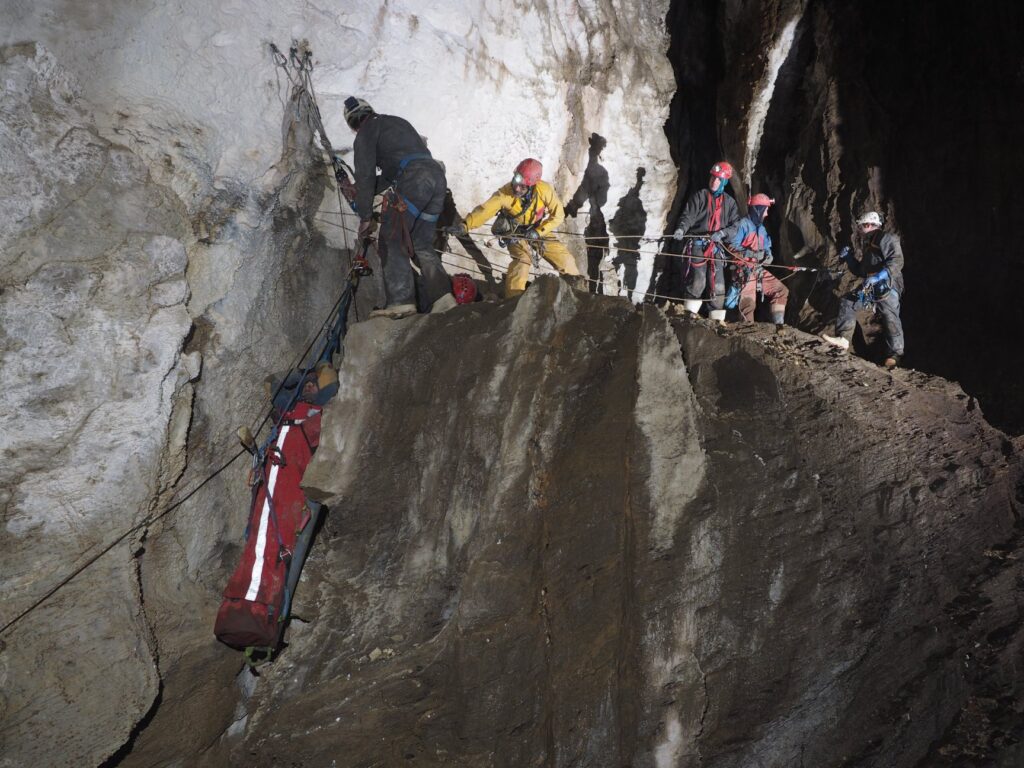 This photo shows a group of rescuers lowering a persion in a stretcher off a cliff face using specialist ropes.